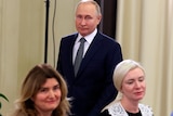 Three women look on as Vladimir Putin stands behind them