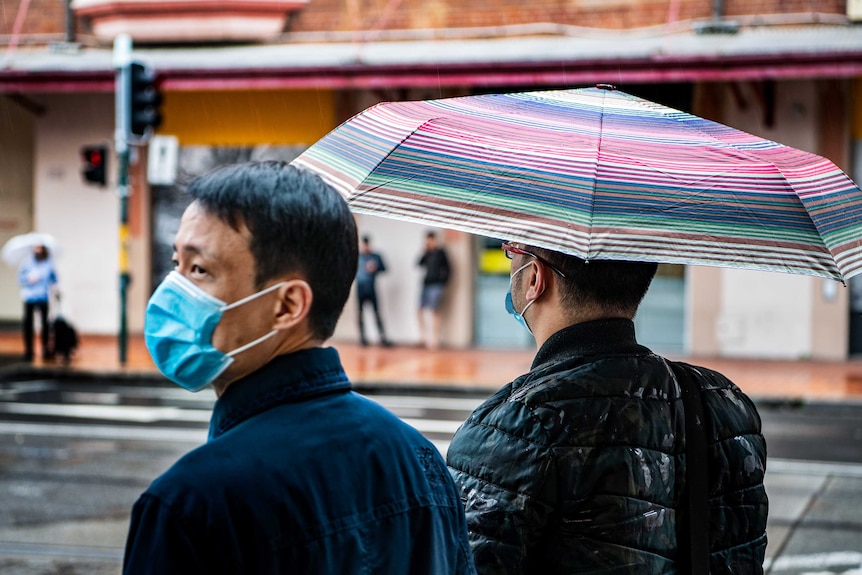 Two men wearing masks walk stand in a street in the rain.