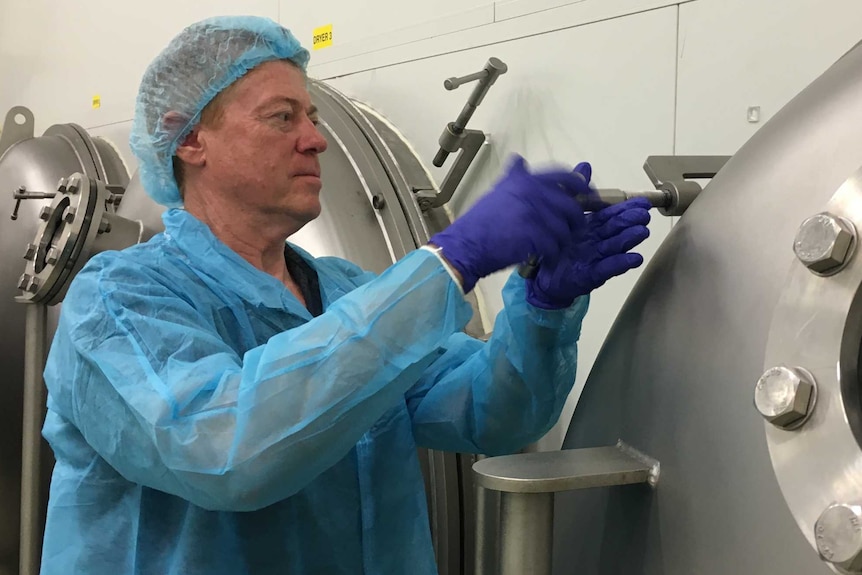 Michael Buckley locks large circular dryer door dressed in hospital-style scrubs.