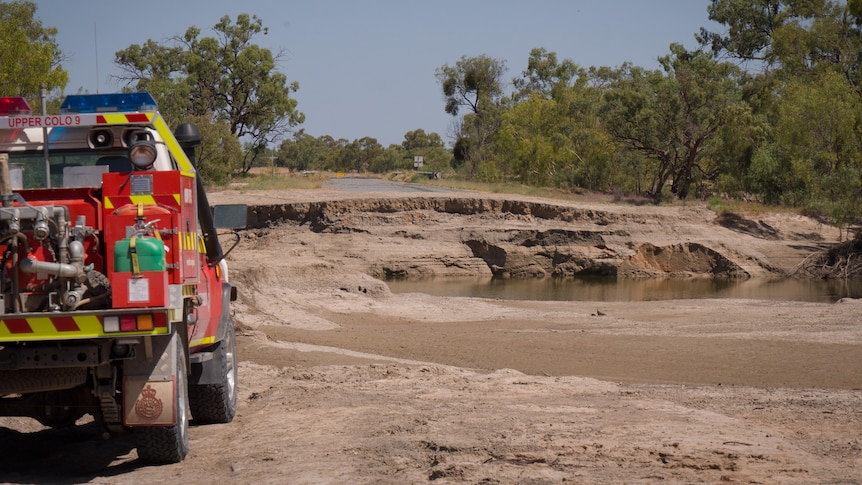 A State Emergency Service vehicle parked facing a large hole the has formed in the middle of a roadway in an arid landscape.