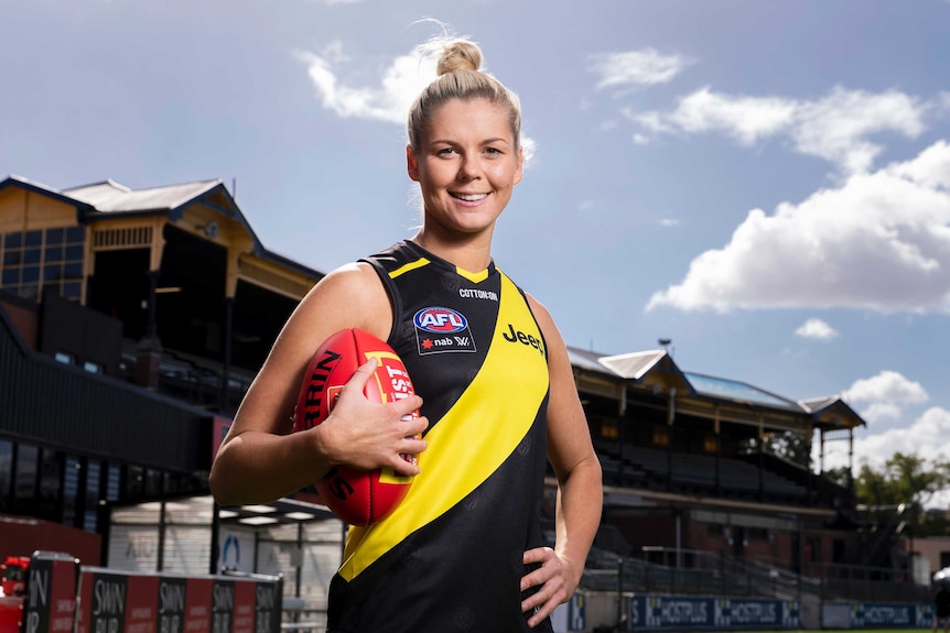 An AFLW player stands holding a football in the colours of her new team.