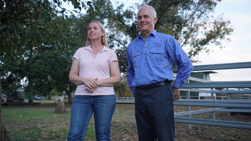 A woman wearing jeans and a pink t-shirt stands next to a man wearing a shirt and pants.