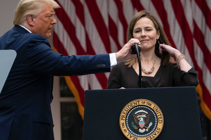 President Donald Trump adjusts a microphone for Judge Amy Coney Barrett at a podium