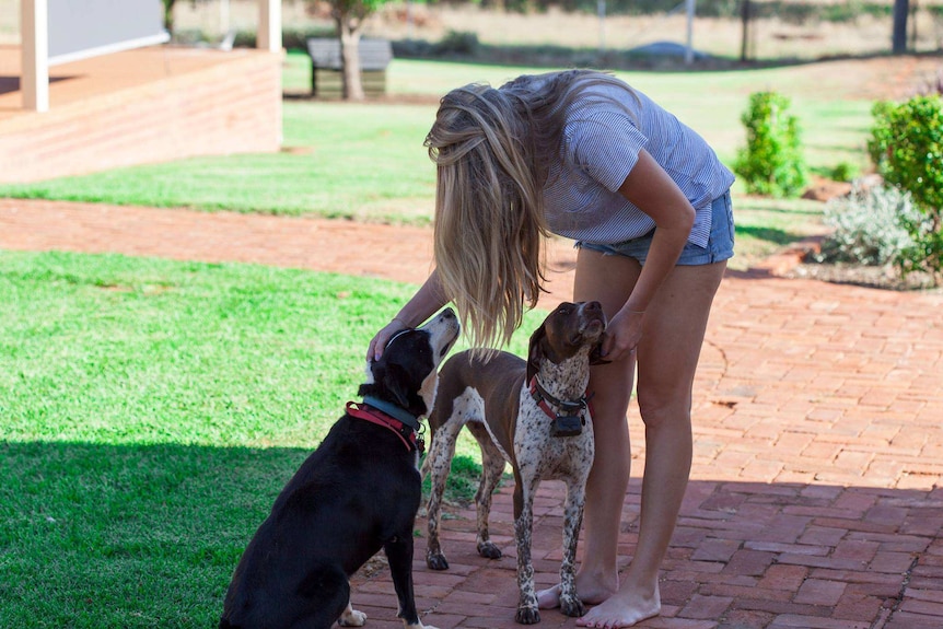 Rachel Bragg in a backyard with two dogs sitting in front of her.