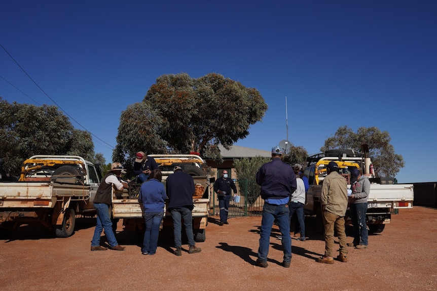 People wearing jeans and hats wait with utes in front of a building