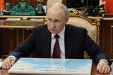 Russian President Vladimir Putin sits at a desk with his hands on it.