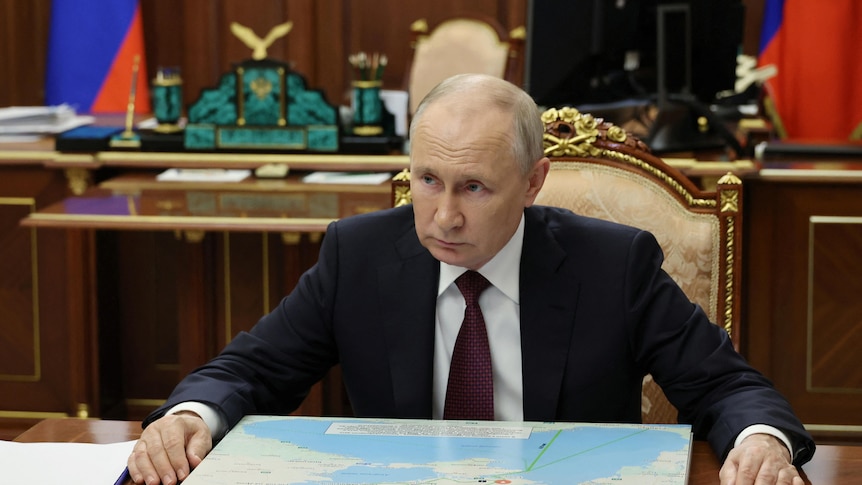 Russian President Vladimir Putin sits at a desk with his hands on it.