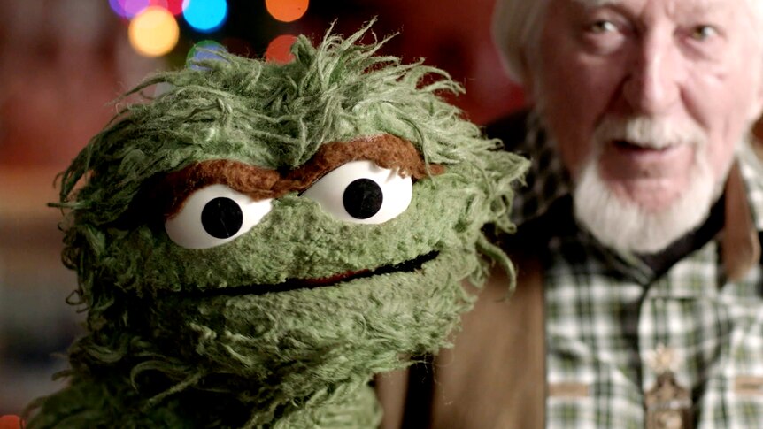 Oscar the Grouch in front-left with Caroll Spinney behind the muppet.