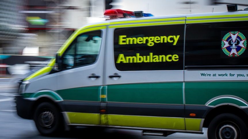 A green and white ambulance with a blurred street behind it