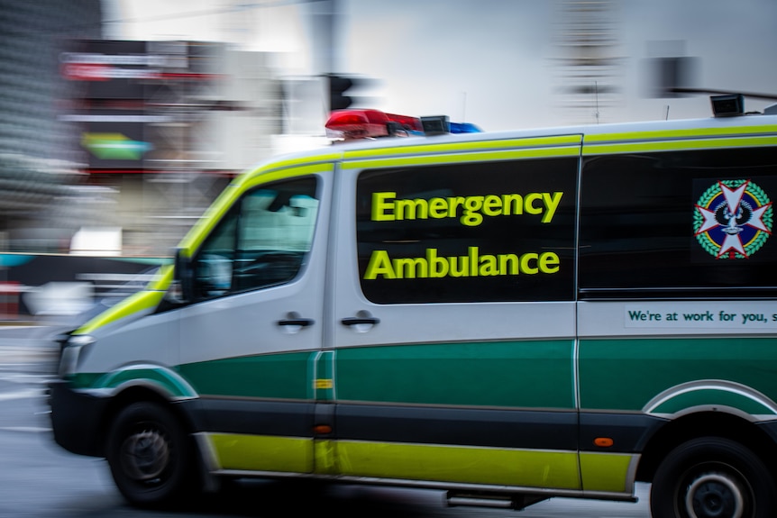 A green and white ambulance with a blurred street behind it