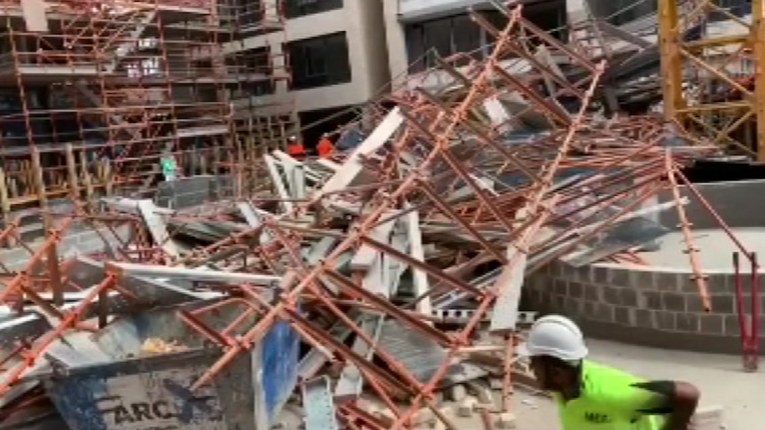 Fallen scaffolding is piled up over the ground as a worker in a hard hat runs for safety.