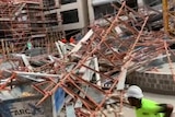 Fallen scaffolding is piled up over the ground as a worker in a hard hat runs for safety.