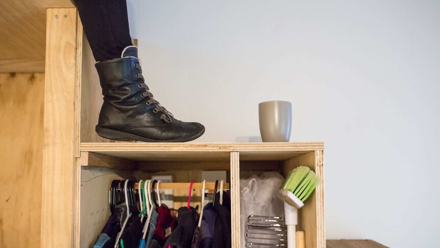 Clothes and cleaning equipment is stored under the stairs of the tiny house.