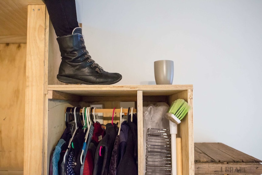 Clothes and cleaning equipment is stored under the stairs of the tiny house.