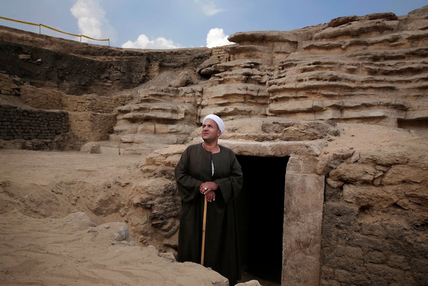 The leader of the excavation stands in front of a newly discovered tomb.