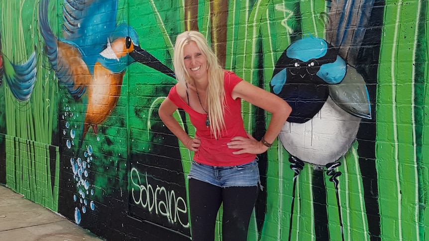 A woman leans against a  mural