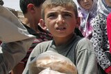 A Syrian boy carries bags of bread as people queue up outside a bakery in the northern town of Aldana