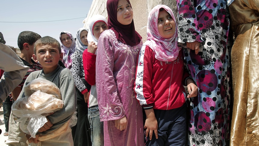 A Syrian boy carries bags of bread as people queue up outside a bakery in the northern town of Aldana