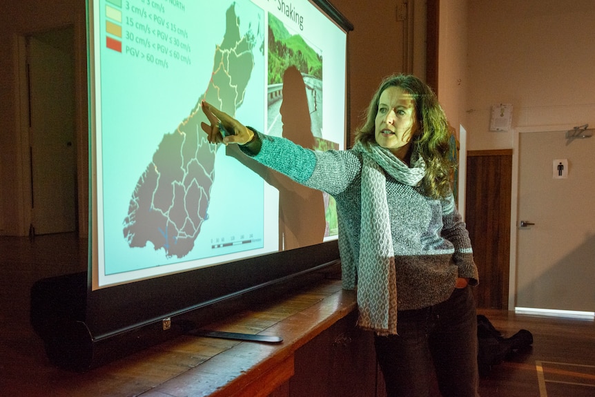 Caroline points to the Whataroa area on a map as the projector light shines on her face. 