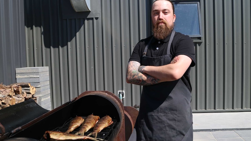 a chef stands in front of a large grill used to smoke fish