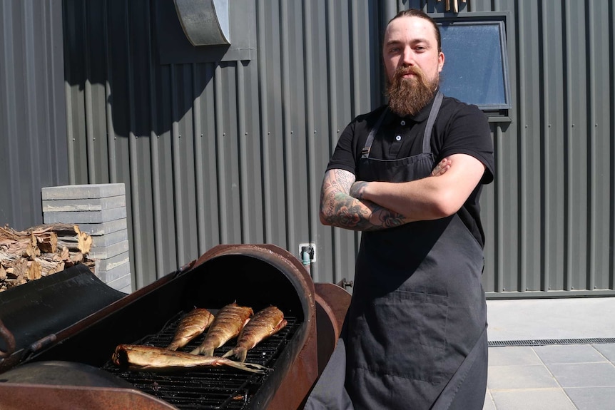 Chef stands in front of a large grill used to smoke fish