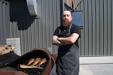 a chef stands in front of a large grill used to smoke fish