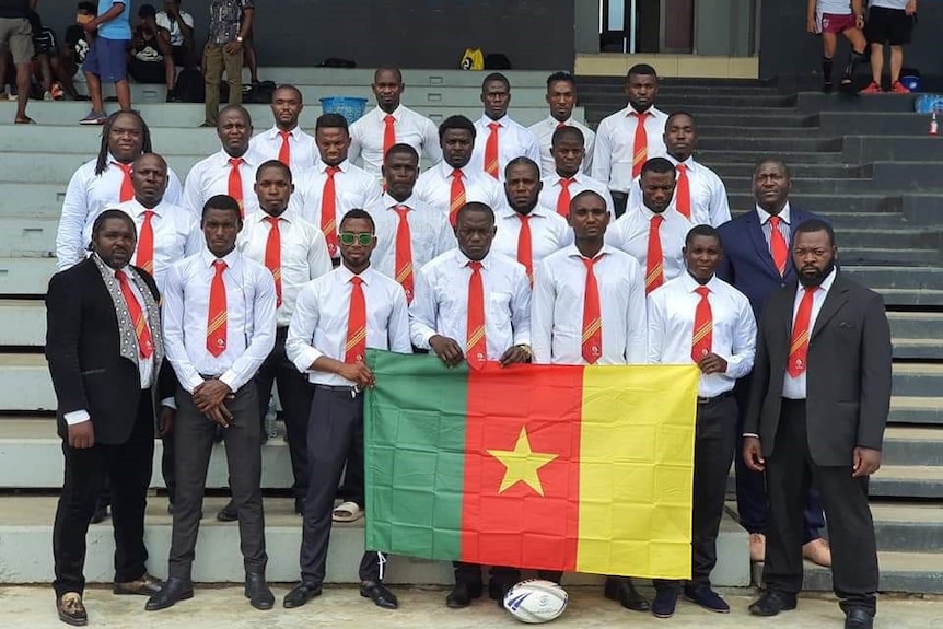 A group of rugby league players pose behind a Cameroonian flag