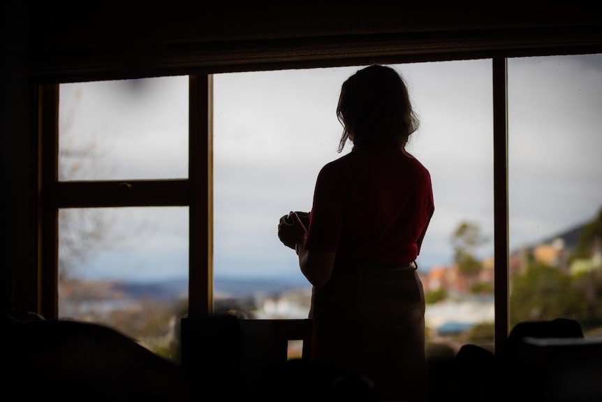 silhouette of a woman looking out a window holding a coffee cup 