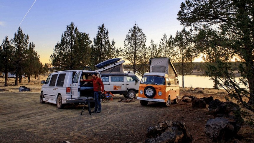 Three vans parked in front of a lake.