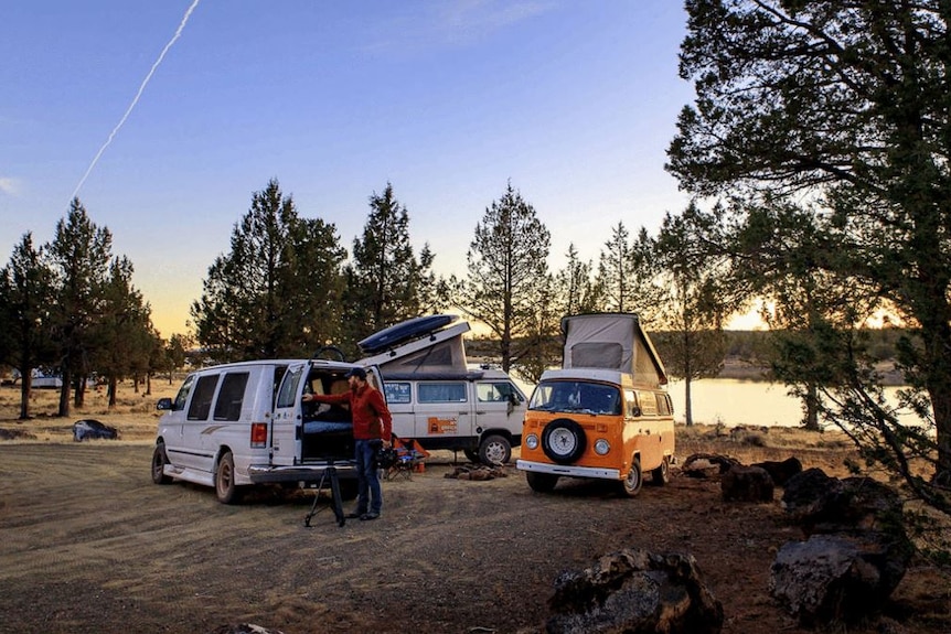 Three vans parked in front of a lake.