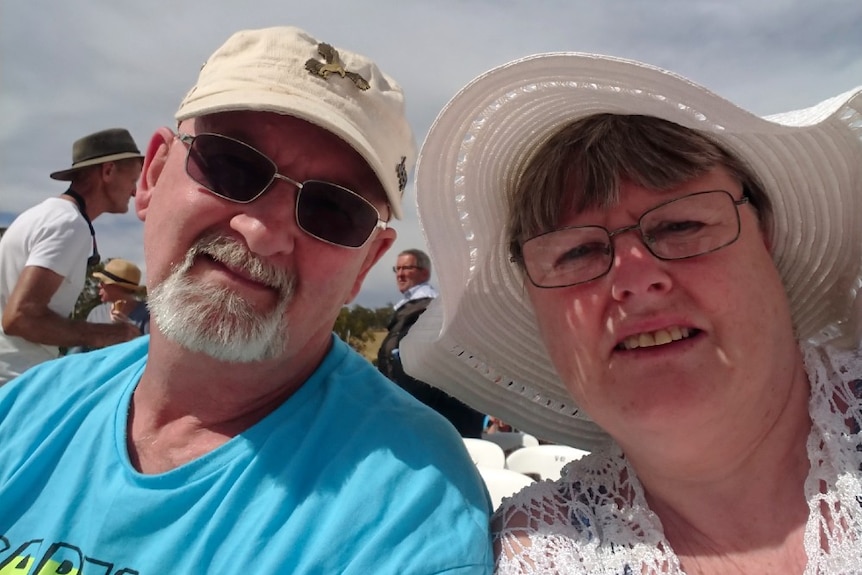 Caren Ruck and her husband smile for a selfie outdoors in the sunshine.