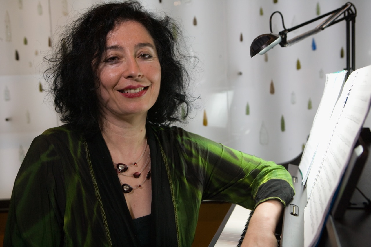 Composer Elena Kats-Chernin sitting at piano with green shirt on.