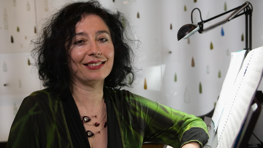 Composer Elena Kats-Chernin sitting at piano with green shirt on.