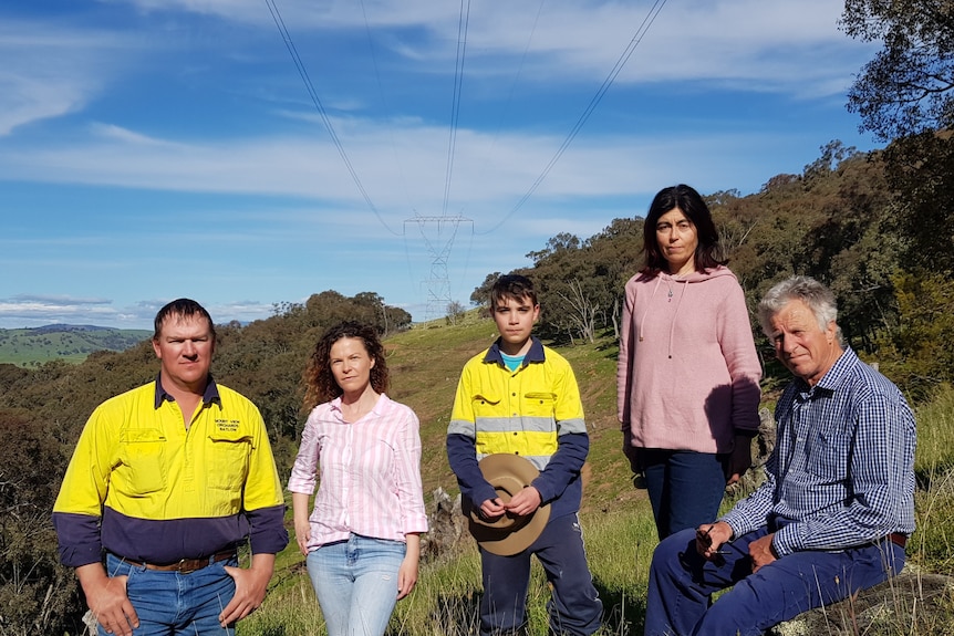 Group of people stand with powerlines and hills in background.