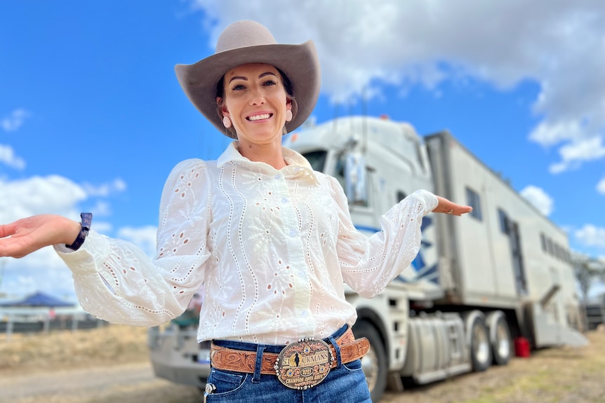 A woman in a hat and white long sleeved shirt poses in front of her very big truck