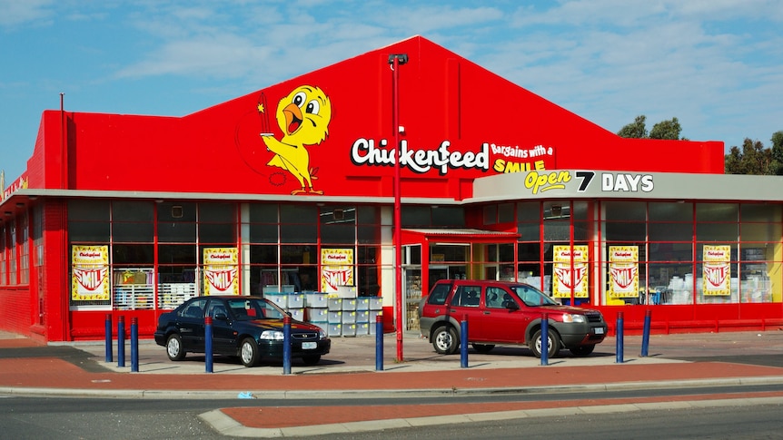 The exterior of a store, painted entirely in red, with the word Chickenfeed in bold writing next to a yellow cartoon chicken.