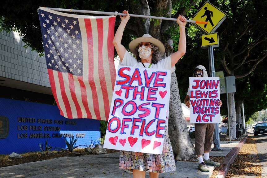 A woman waving a flag wearing a sign that says 'save the post office'