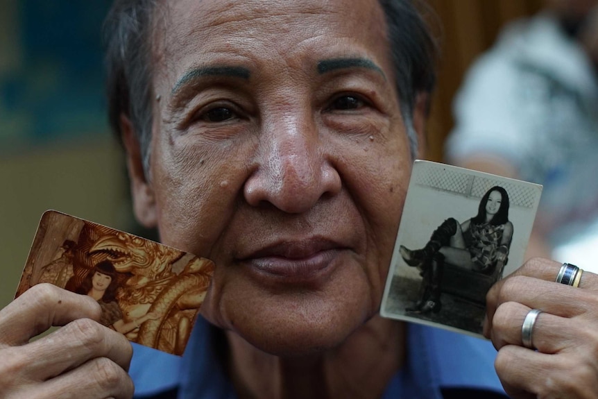 Transgender woman Pitin holding photographs of herself as a younger waria.