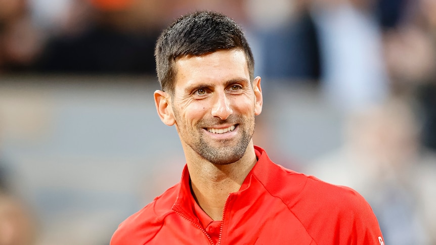 Novak Djokovic smiles wearing a red top