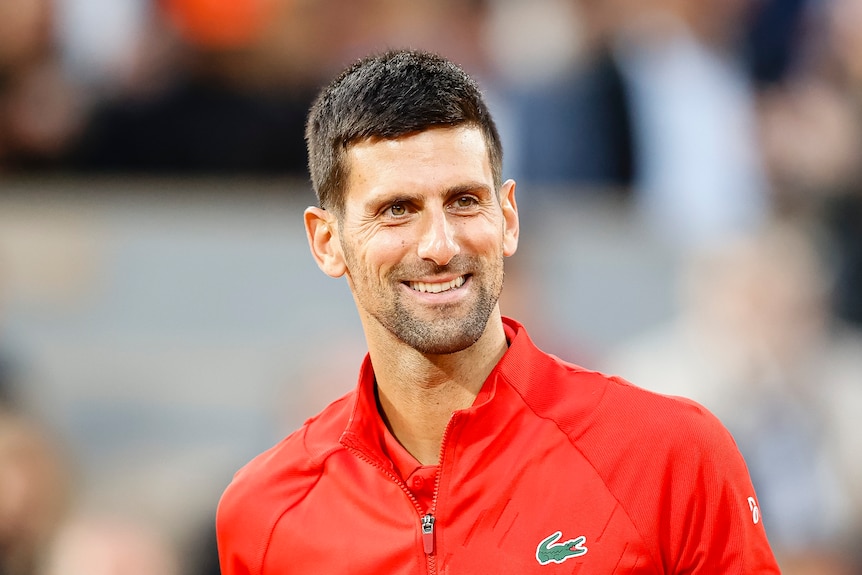 Novak Djokovic smiles wearing a red top