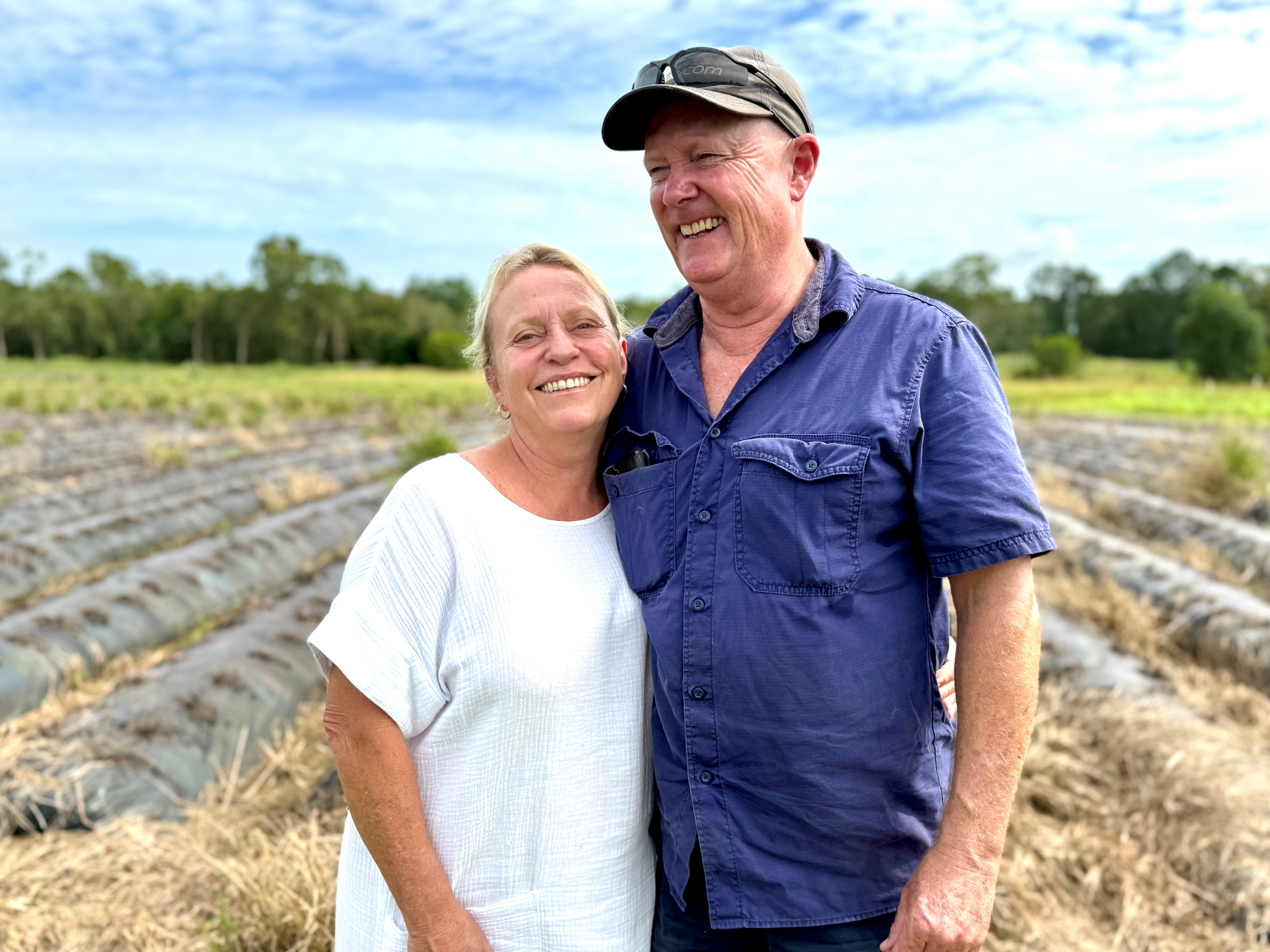 A smiling couple in front of a disused strawberry field.