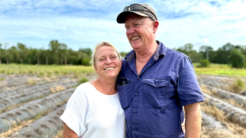 A smiling couple in front of a disused strawberry field.
