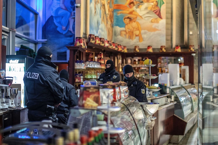 Four masked police officers stand in an ice cream parlour.