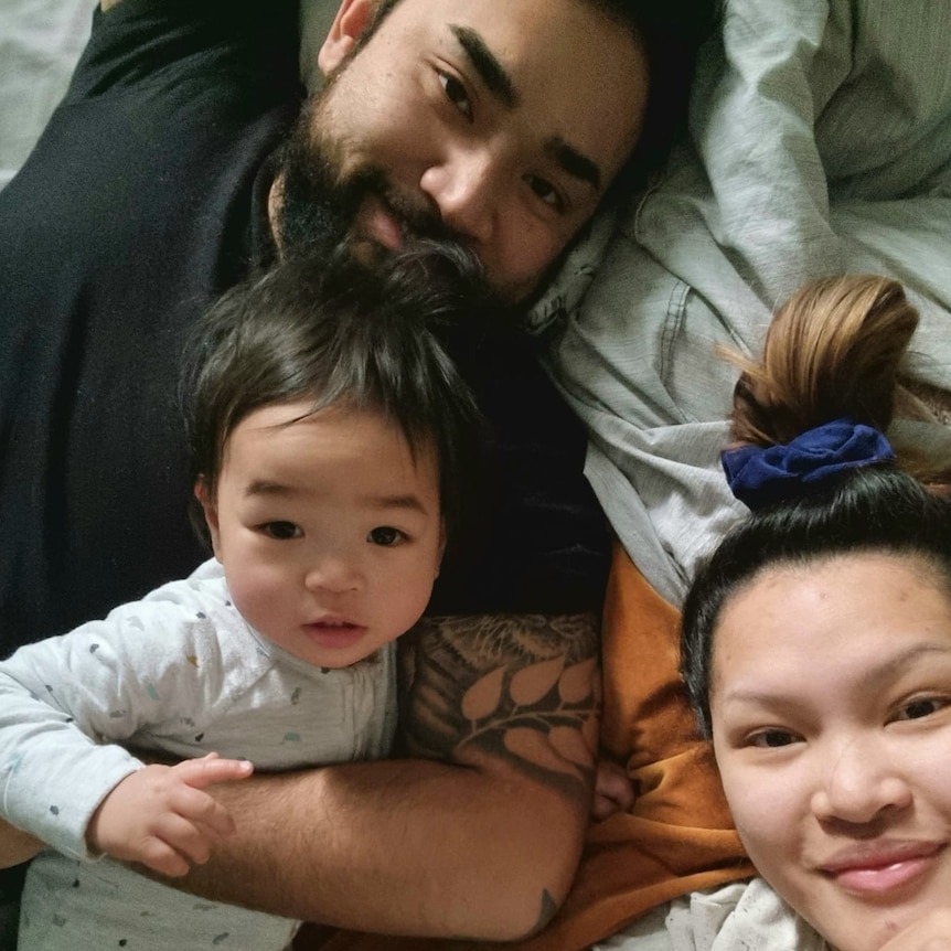 Emma and Beato lie in bed and take a selfie with their baby, Koa.