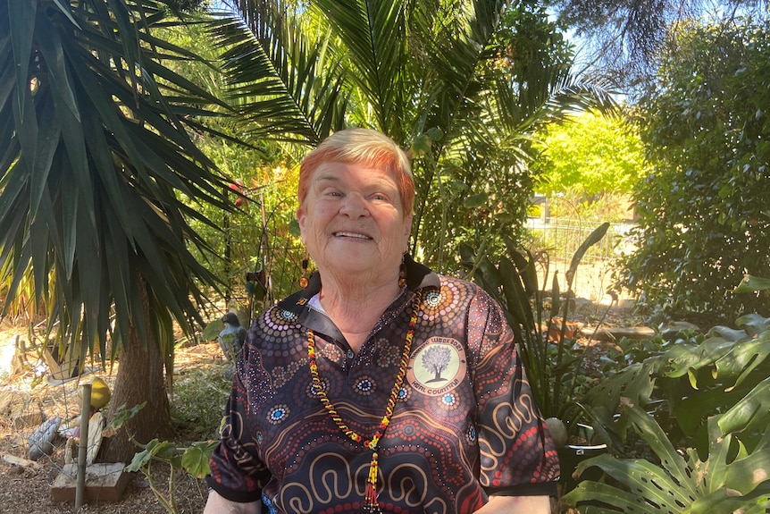 A woman with short ginger and blonde hair looks and smiles at camera, she's wearing a NAIDOC t shirt.