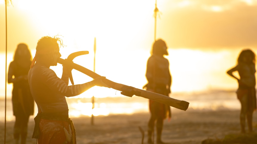 Aboriginal man plays didgeridoo with a sunset in the background