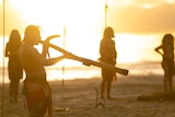 Aboriginal man plays didgeridoo with a sunset in the background