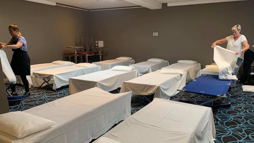 A number of cots lined up covered in white bed sheets inside the dining room of a pub