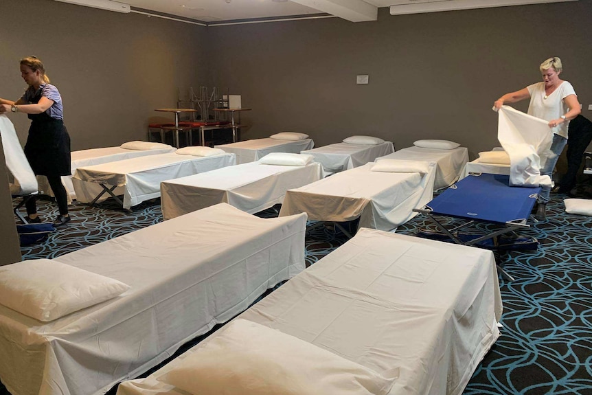 A number of cots lined up covered in white bed sheets inside the dining room of a pub