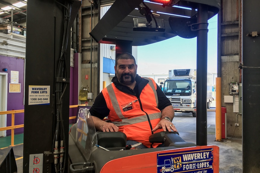 A man in highvis vest sits on a forklift in a warehouse